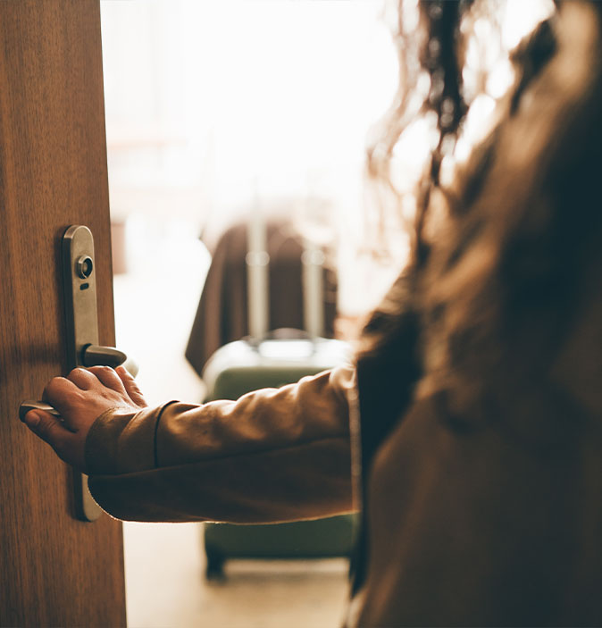 Anonyme Person mit Hand an der Türklinke einer geöffneten Tür.