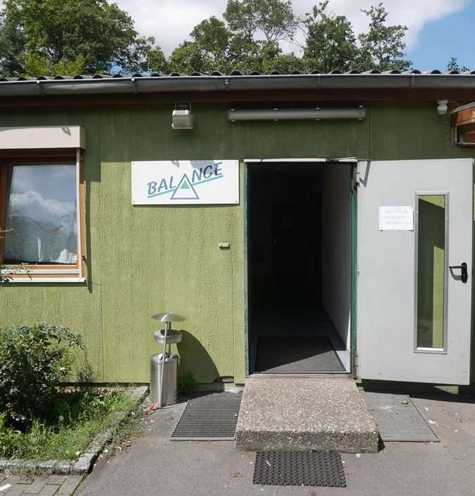 Eingang des Café Balance. Grünes Gebäude, graue Tür