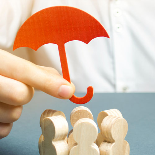 Eine Hand, die einen orangenen Papierschirm über eine im Kreis angeordnete Gruppe von kleinen Holzpuppen hält.