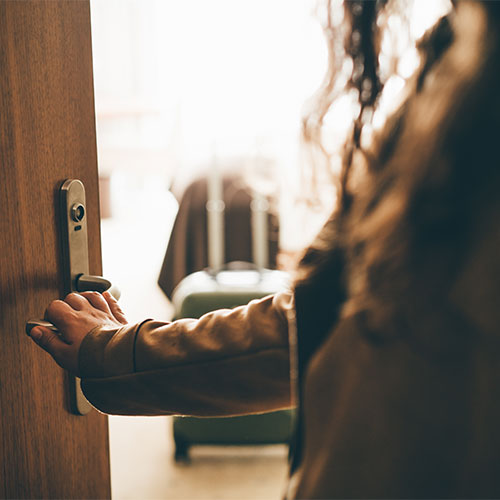 Anonyme Person mit Hand an der Türklinke einer geöffneten Tür.