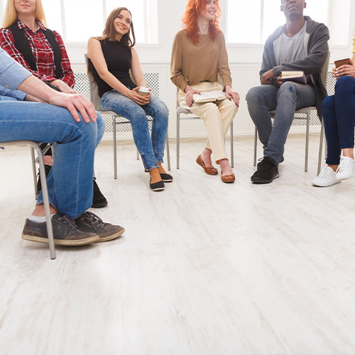 Eine Gruppe von Personen, die auf Stühlen in einem Halbkreis sitzen und sich unterhalten.