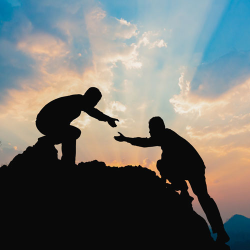 Silhouetten zweier Männer die sich beim Überwinden eines Hindernisses die Hand reichen