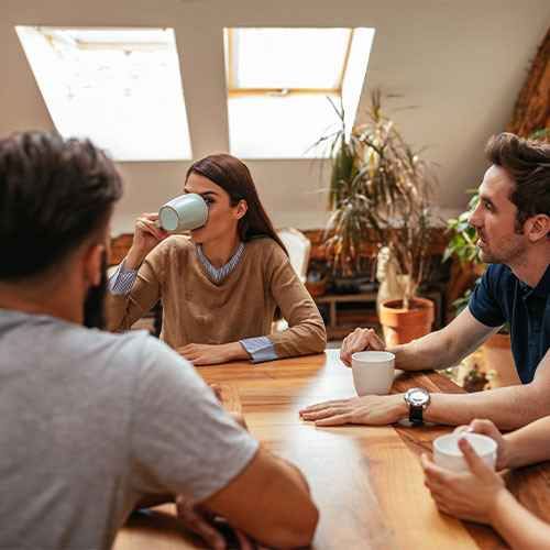 Mehrere Personen an einem Esstisch, die sich unterhalten und Kaffee trinken.